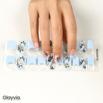 Hand wearing Glayvia NG200019 blue petal French semi cured gel nail wraps displayed above matching blue French floral nail wrap sticker sheet