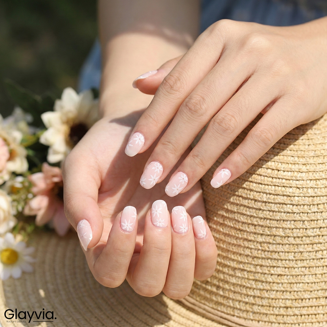 Lifestyle image of Glayvia NG200032 soft daisy blush semi cured gel nail wraps with pale pink floral manicure holding straw summer hat
