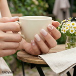 Lifestyle image of Glayvia NG200210 Dainty Daisies semi cured gel nail wraps with delicate white daisy nail art holding a coffee cup in garden setting